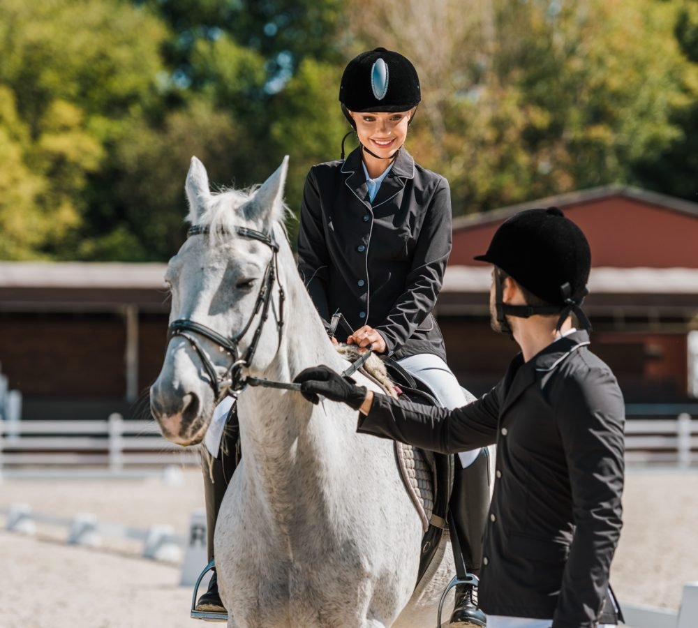 male-equestrians-holding-horse-halter-female-jockey-sitting-on-horse-at-horse-club.jpg male-equestrians-holding-horse-halter-female-jockey-sitting-on-horse-at-horse-club.jpg